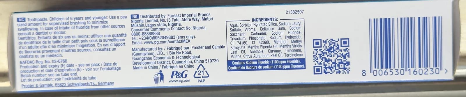 The long side panel of a toothpaste carton with the P&G logo: warnings in two languages, the NAFDAC number, the manufacturer, the ingredients list, a QR code and a barcode.